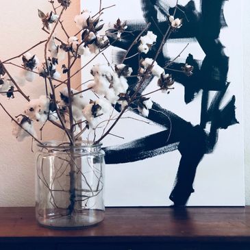 Cotton stems in a glass jar against abstract art.