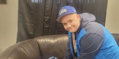 A man wearing blue jacket and cap smiles indoors.