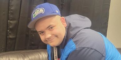 A man wearing blue jacket and cap smiles indoors.