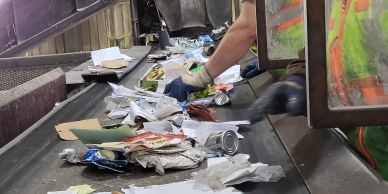 Worker sorting items on a conveyor belt at a recycling center.