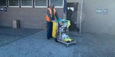 Janitor with cleaning cart outside a building.