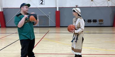 Two people in costumes holding basketballs on a court.