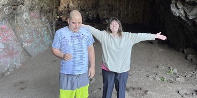 Two people standing at a graffiti-covered cave entrance.