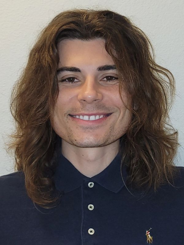 Young man with long brown hair smiling in a navy polo shirt.