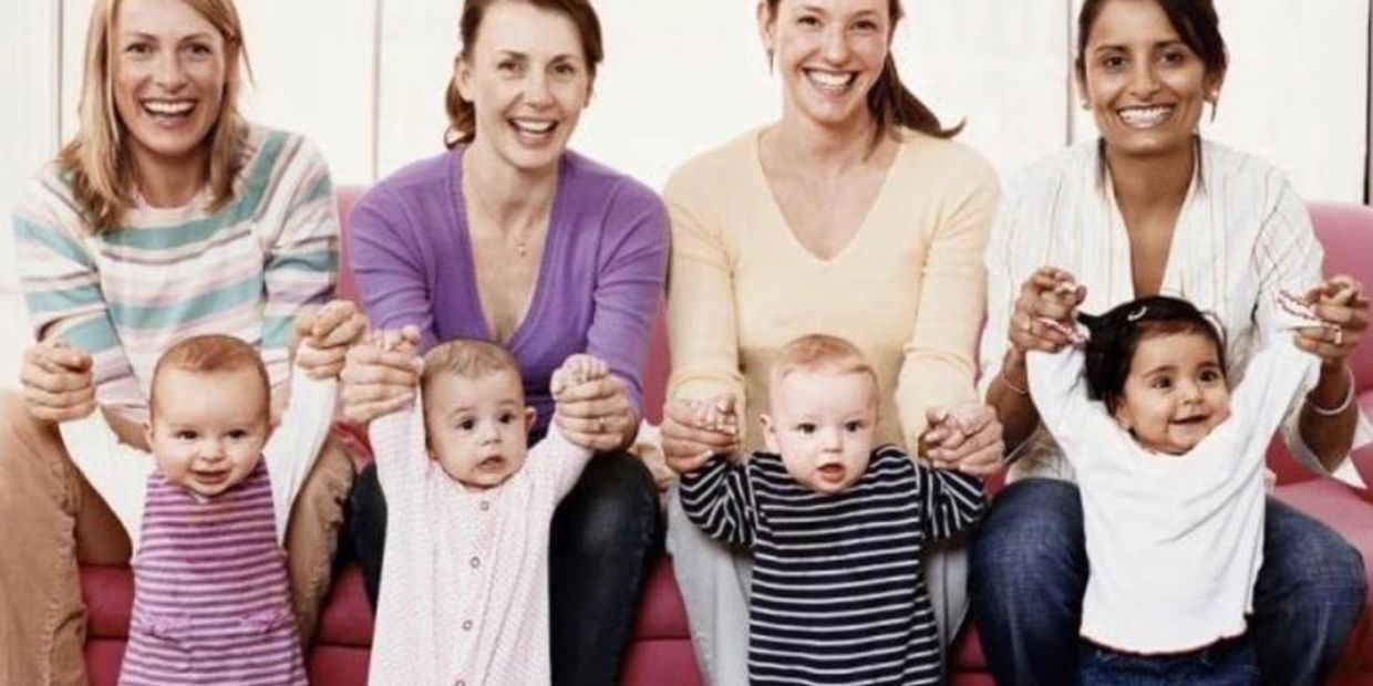 Four mothers holding hands of their babies smiling.