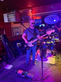 Musician playing bass guitar on stage in a dimly lit venue.