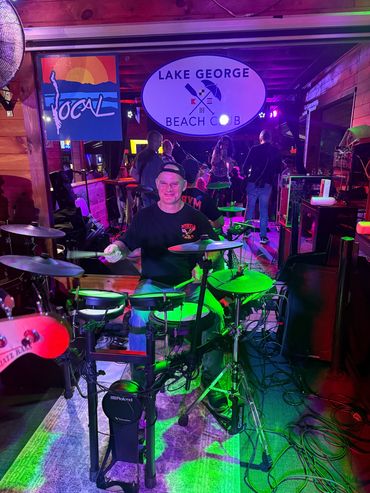 A smiling drummer playing an electronic drum set at a live venue.