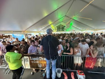 DJ performing at a crowded outdoor event under a tent.