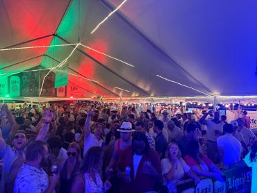 Crowded party inside a large tent with colorful lights.