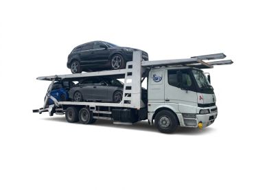 A white car transporter truck carrying two dark-colored cars.