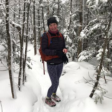 A woman smiling while hiking in a snowy forest trail.