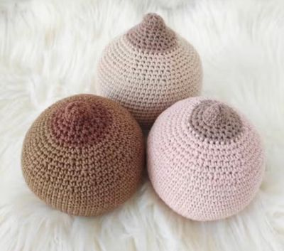 Three crocheted breast models in varying skin tones on a white surface.