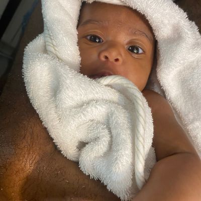 A baby wrapped in a white towel looking up with wide eyes.