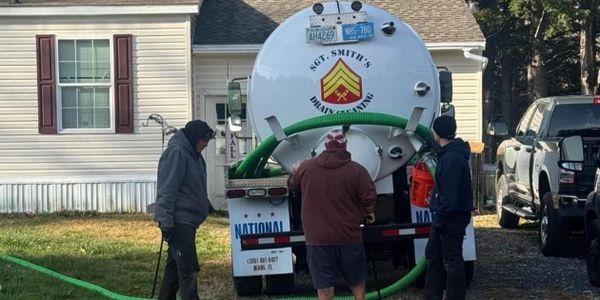 Three men working with a septic tank service truck in a residential area.
