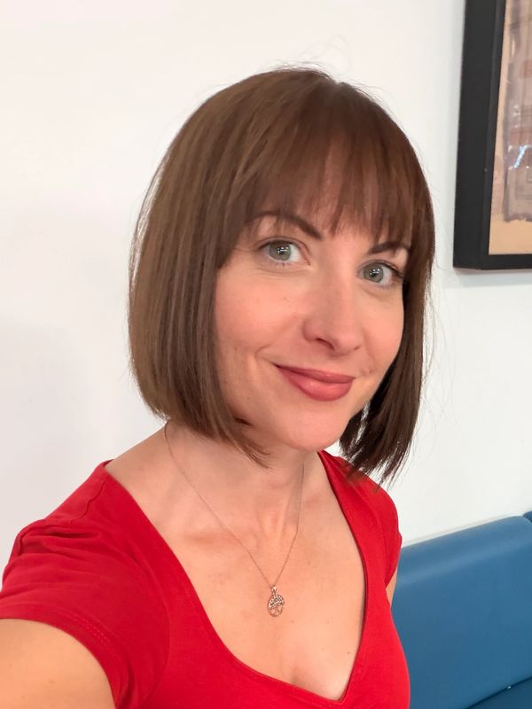 Woman in red top smiling, sitting by a coffee.