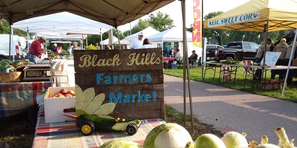 Farmers market stand with fresh produce and a wooden sign.