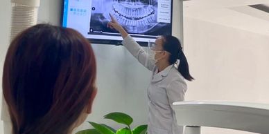 Dentist explaining dental X-ray results to a patient on a wall-mounted screen.
