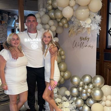 Three people posing at a baby shower with white and gold balloons.