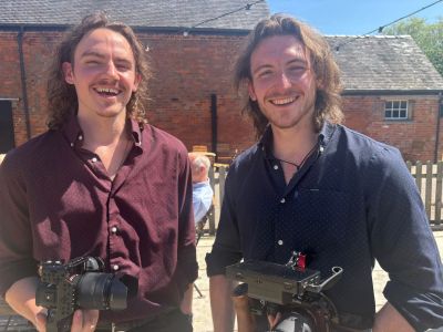 Two smiling men holding camera equipment outdoors.