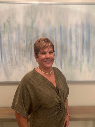 A woman smiling in a green dress with a necklace in front of abstract art.