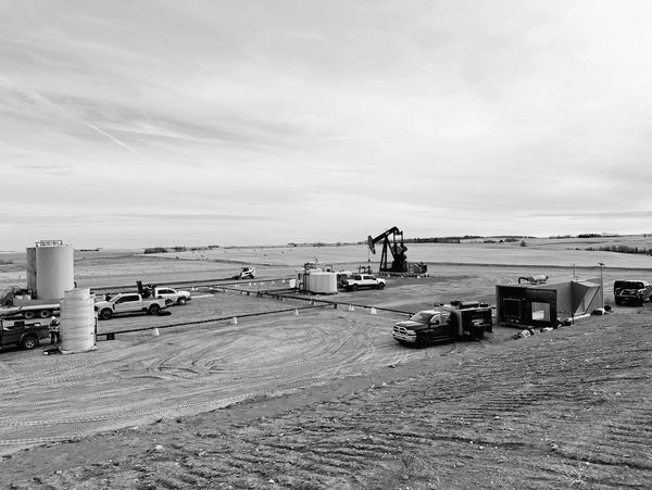 Oilfield site with pumpjack and service trucks in a rural area.