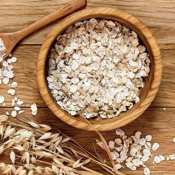 A wooden bowl filled with rolled oats and a wooden spoon on a wooden surface.