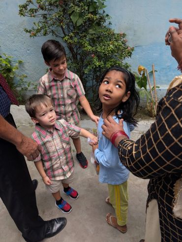 Three children holding hands guided by adults outside.