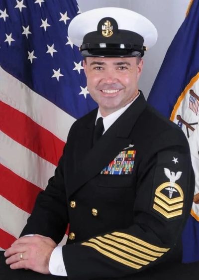 U.S. Navy officer in dress uniform posing with flags in background. David Ocheltree