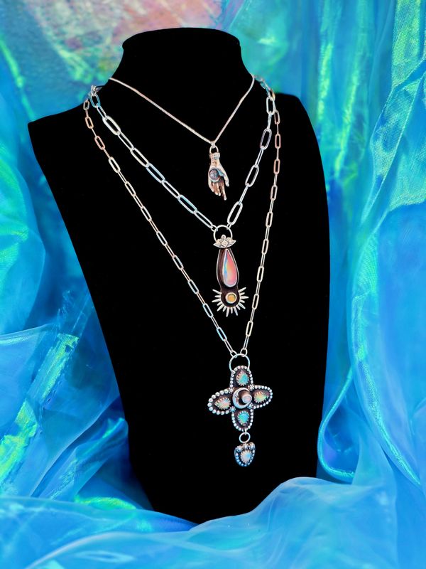 Three silver necklaces with unique pendants displayed on a black bust against a blue fabric background.