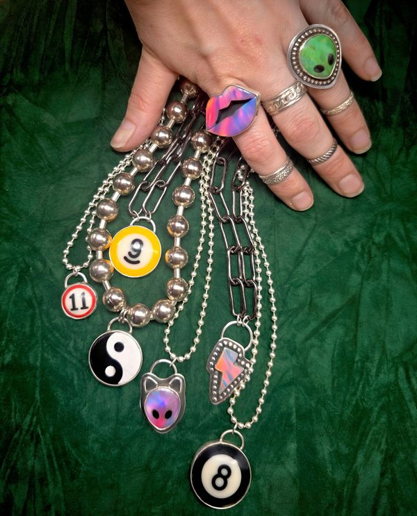 Hand with rings holding various metal necklaces with unique pendants.