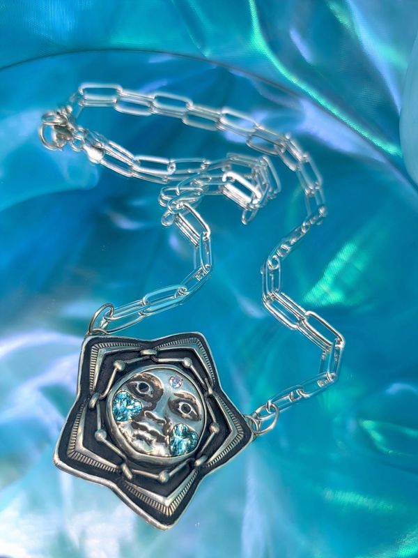 Silver star-shaped pendant with a celestial face adorned with blue gemstones on a silver chain.