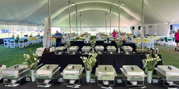 Large outdoor buffet setup under a white tent with chafing dishes and tables.