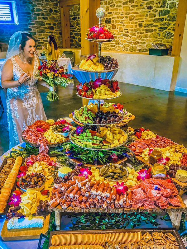 Bride joyfully admires an extravagant charcuterie and fruit display at her wedding.