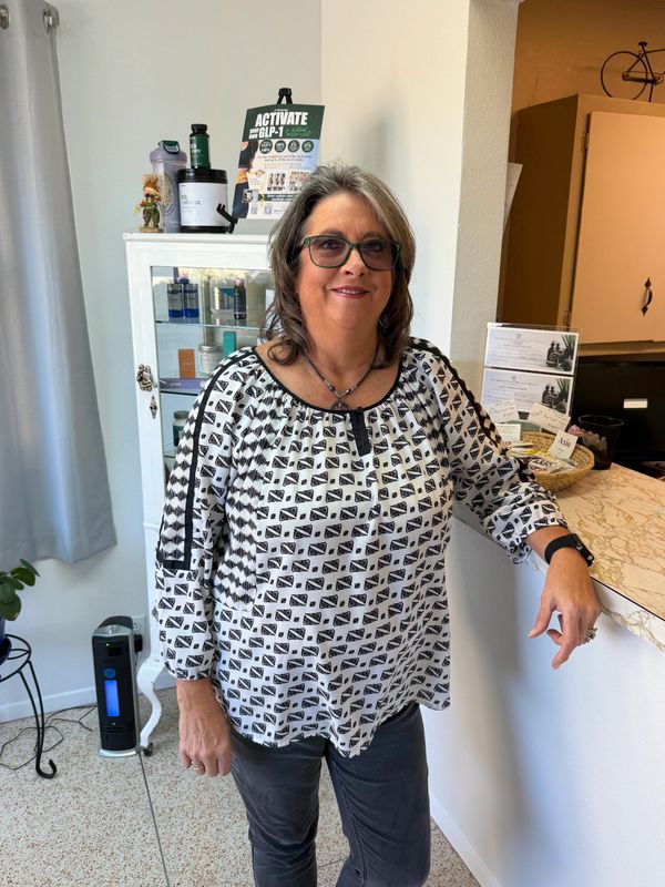 A smiling woman with glasses standing indoors near a counter.