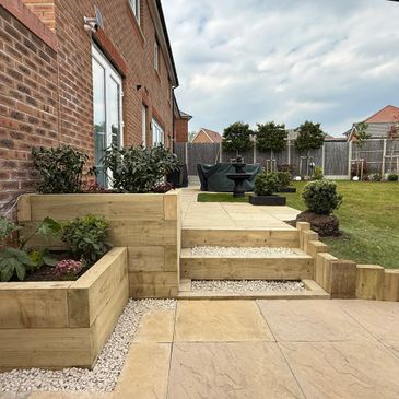 Modern backyard with wooden planters and patio seating area under a cloudy sky.