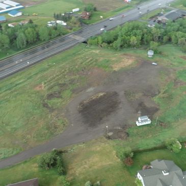 Aerial view of a green field with a small building and a nearby highway.