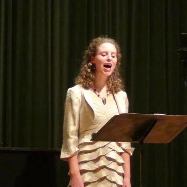 A woman passionately singing on stage with a music stand.