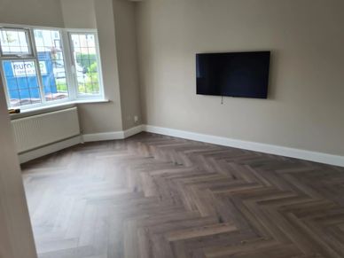 Empty room with herringbone wood flooring and wall-mounted TV.