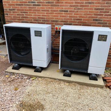 Two white external air conditioning units mounted on a concrete base.