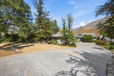 Spacious driveway leading to a house surrounded by trees and mountains.