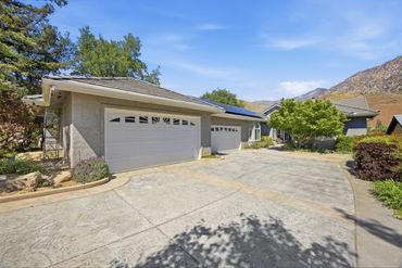 Suburban house with a spacious driveway and two garages under a clear blue sky.