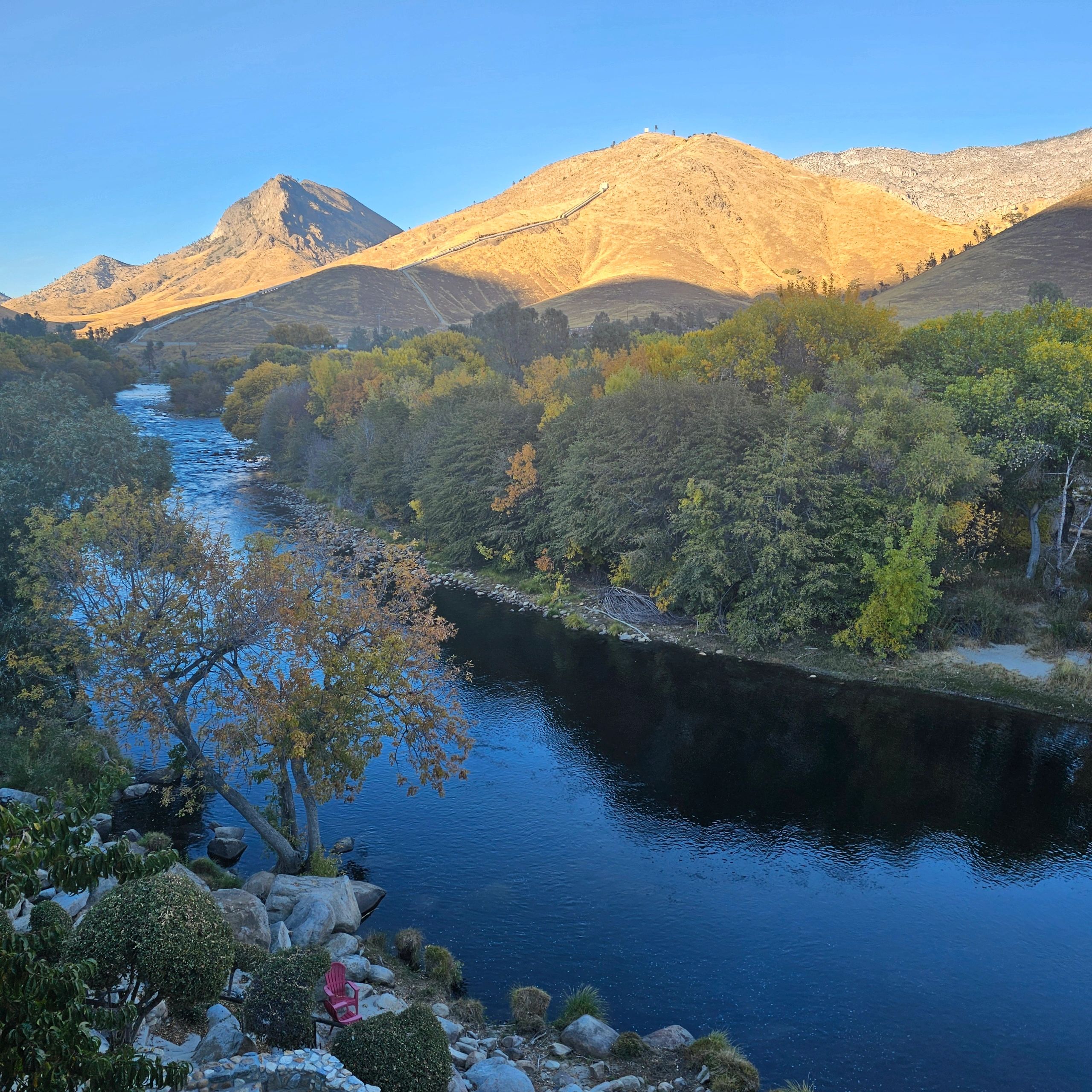 River flowing through autumn-colored trees with golden hills in the background.