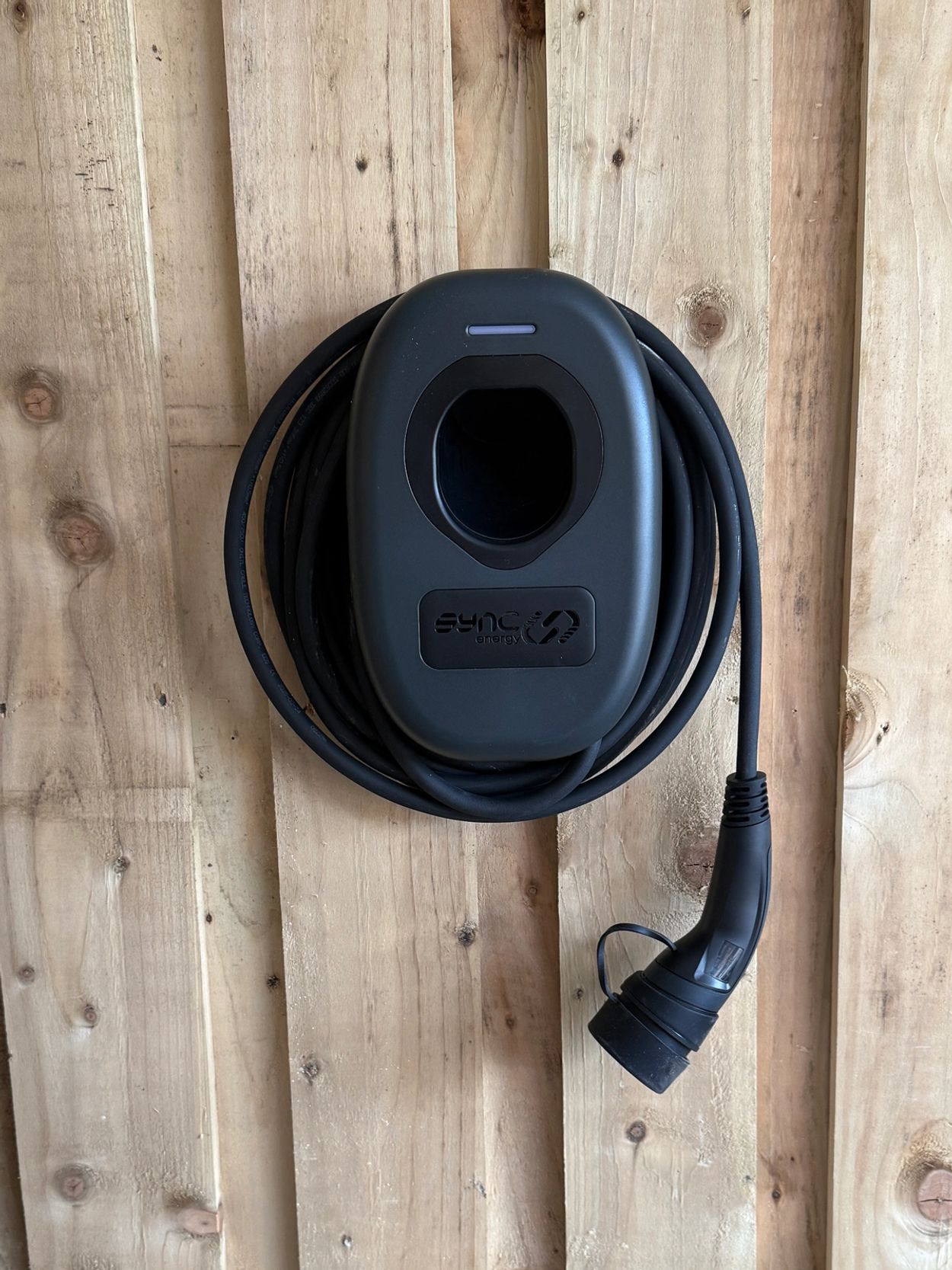 Black electric vehicle charger mounted on wooden wall.