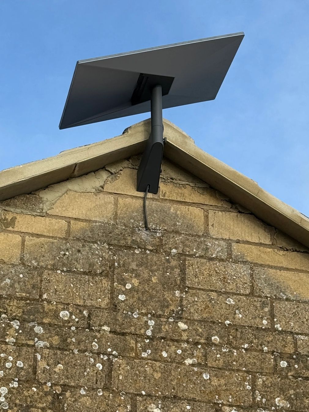 Solar panel mounted on an old brick building under a clear blue sky.