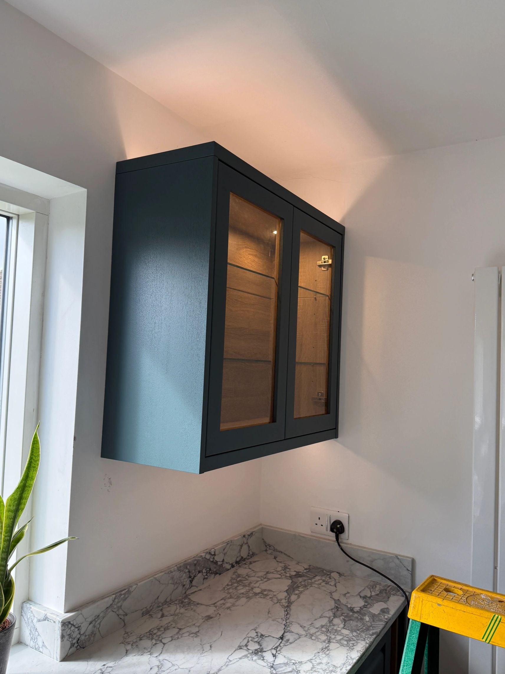 Modern kitchen corner with a dark wall cabinet and marble countertop.