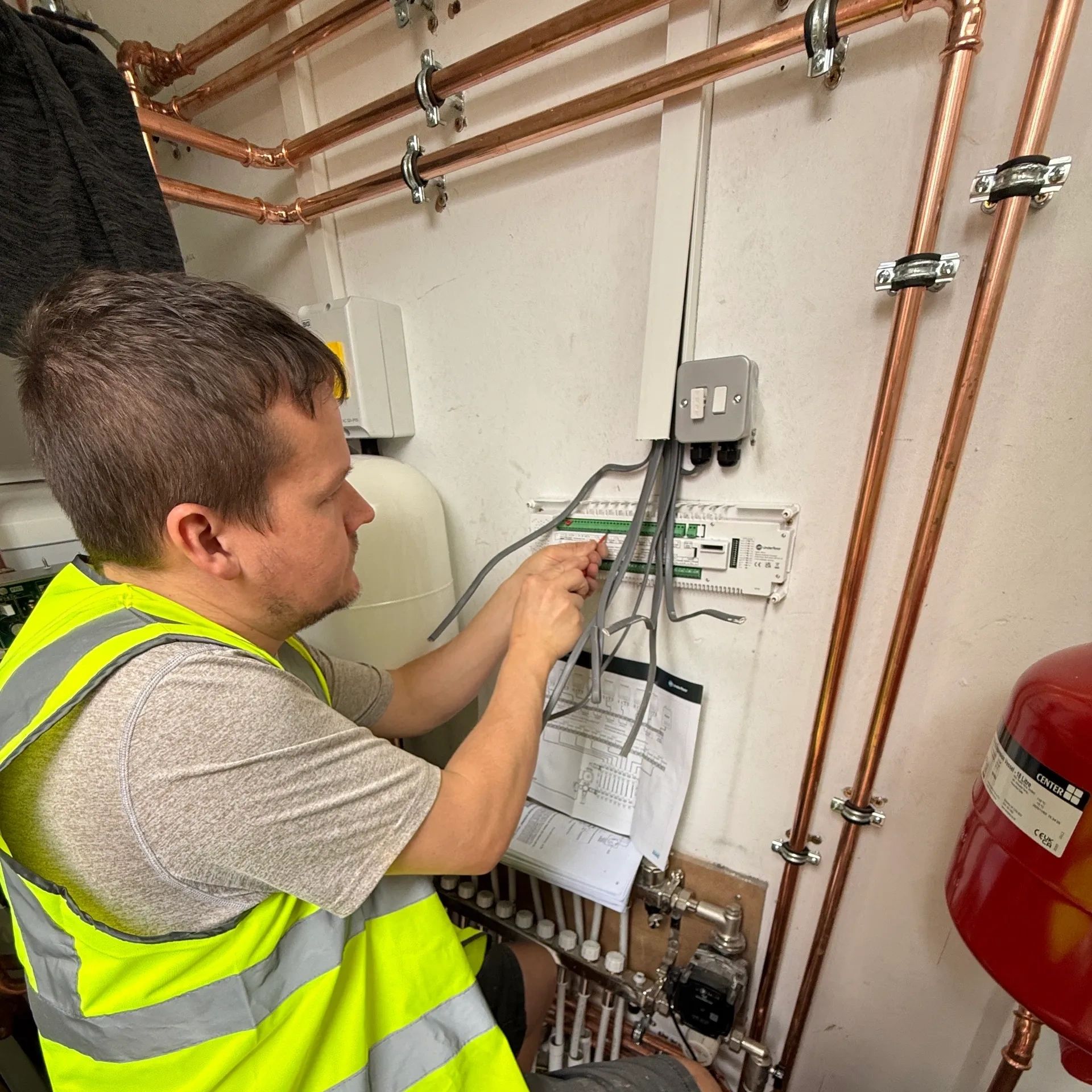 Technician wiring electrical panel with copper pipes around.