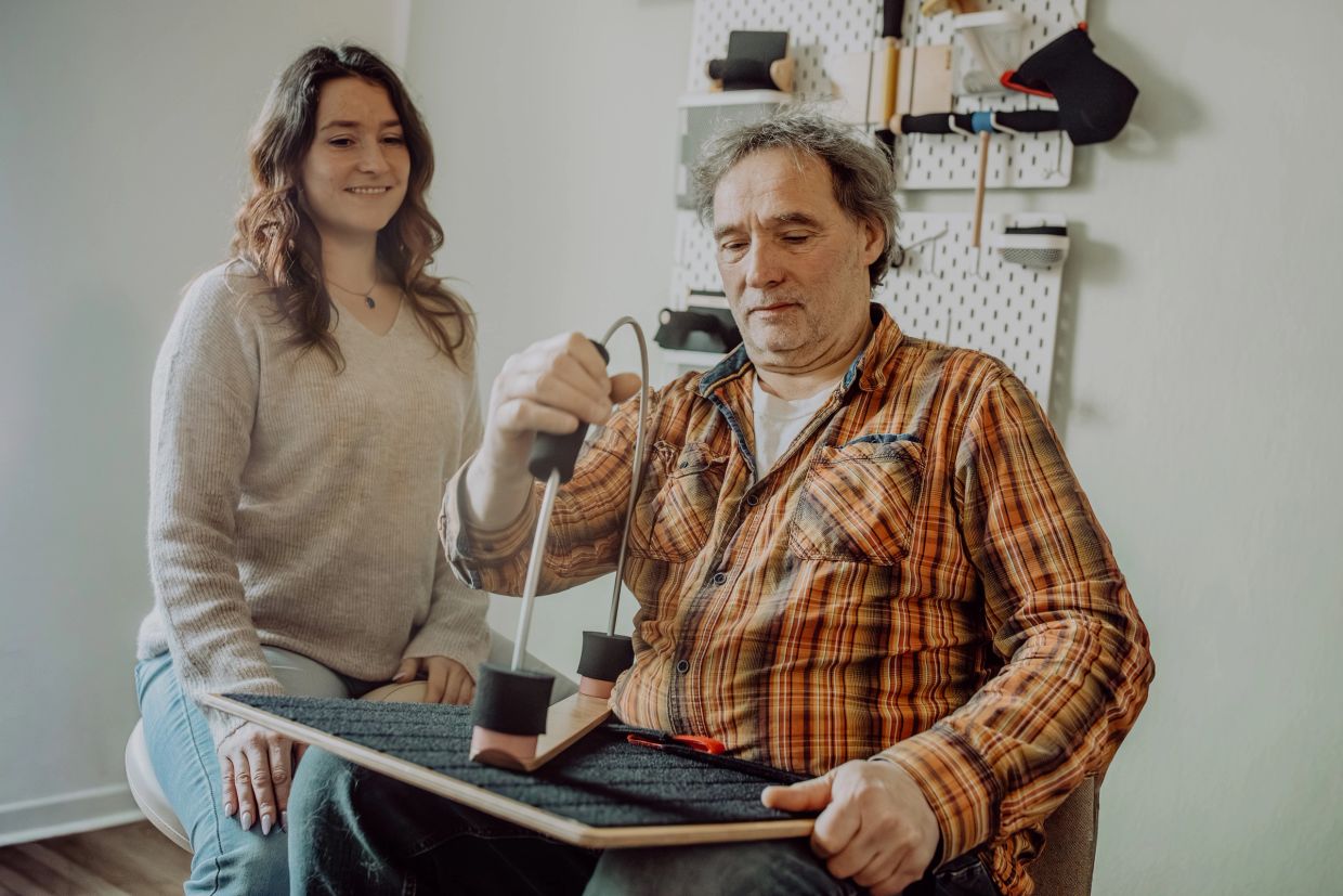 A man uses a rehabilitation device while a woman watches supportively.
