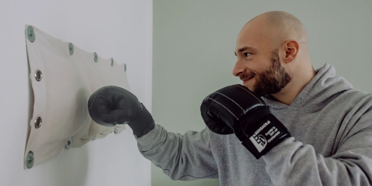 Man in boxing gloves punching a padded wall target indoors.