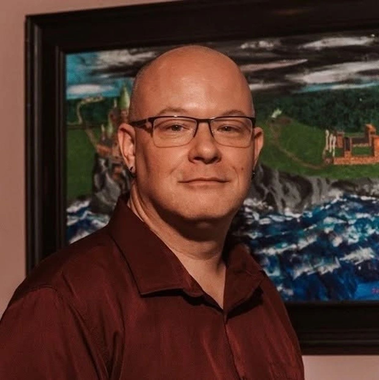 Man with glasses and earrings in front of a colorful painting.