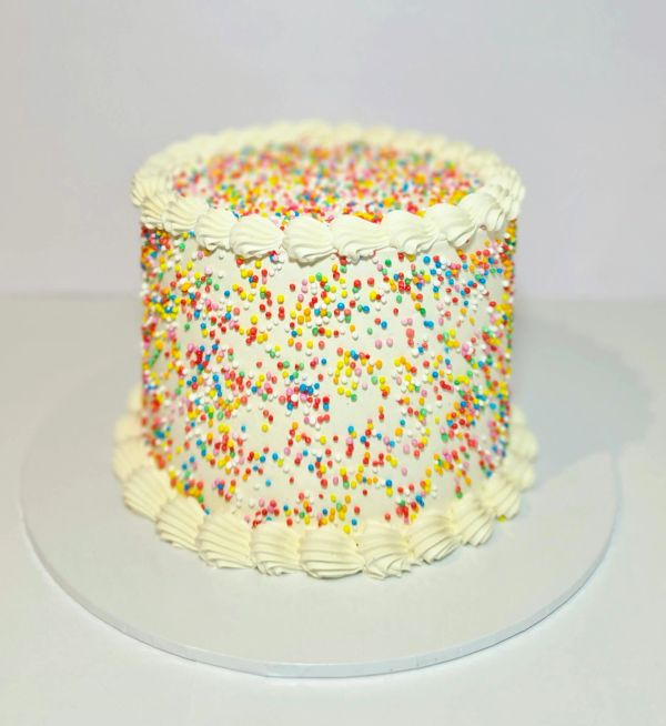 A white cake covered with colorful sprinkles and white frosting swirls.